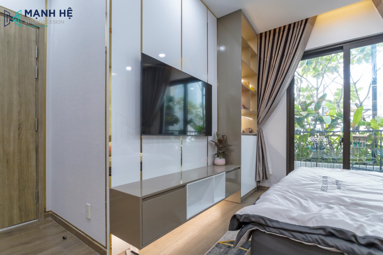 Điểm nhấn đến từ kệ tivi kế hợp tủ trang trí bên hông. Decor thêm các món trang trí cho phòng ngủ thêm sinh động. Tủ quần áo cánh mở cửa kính sang trọng, kết hợp ghế đôn và thảm lót.