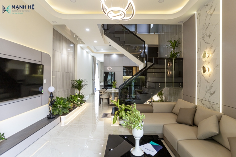 Phòng khách hiện đại liền bếp với trần bo cong và ánh sáng LED hắt, nổi bật bằng các mảng ốp tường vân đá và hệ cầu thang kính