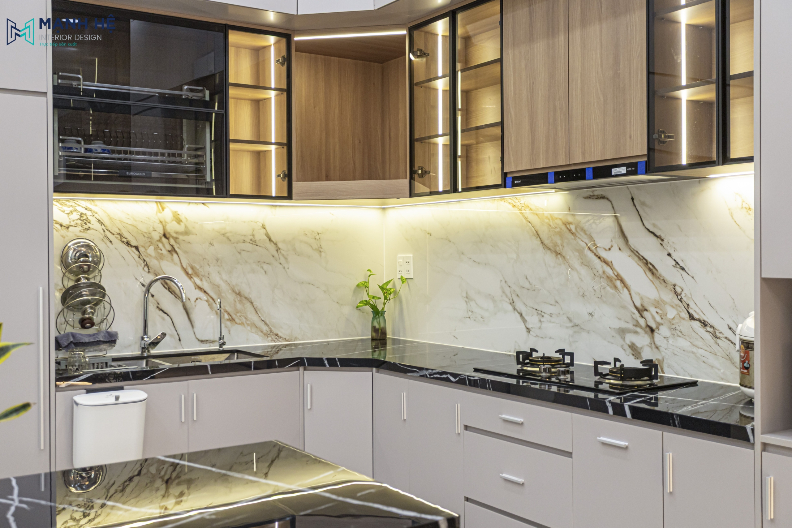 Chi tiết khu vực chậu rửa và bếp nấu trong gian bếp, nổi bật với mặt bếp đá đen, ốp tường bếp vân đá tự nhiên và đèn hắt sáng