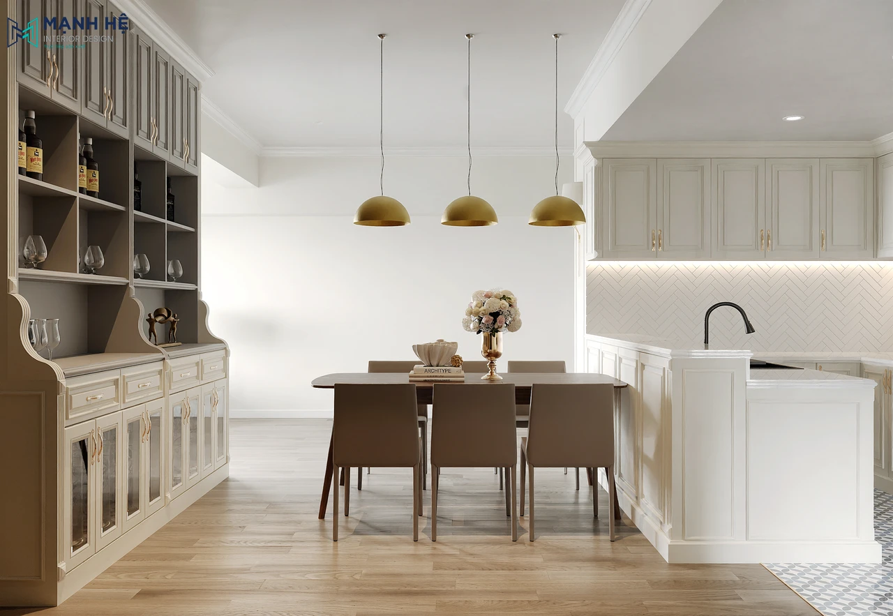 Không gian phòng bếp và phòng ăn phong cách Tân cổ điển với tủ bếp trắng, bàn ăn gỗ đơn giản, đèn thả trần ánh vàng và hệ tủ trưng bày kiểu châu Âu