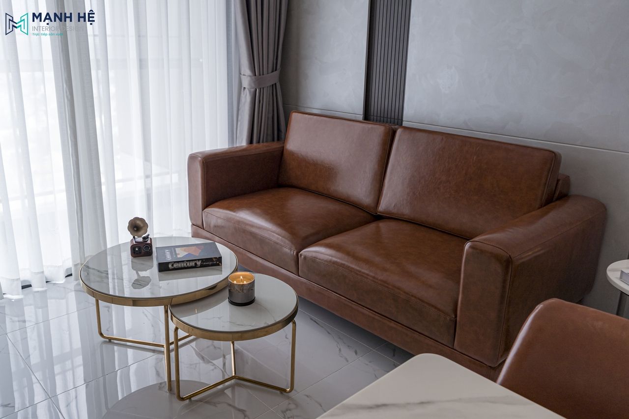 Thi công phòng khách căn hộ với sofa da nâu ấm kết hợp bàn trà đôi mặt đá sang trọng và ánh sáng tự nhiên dịu nhẹ