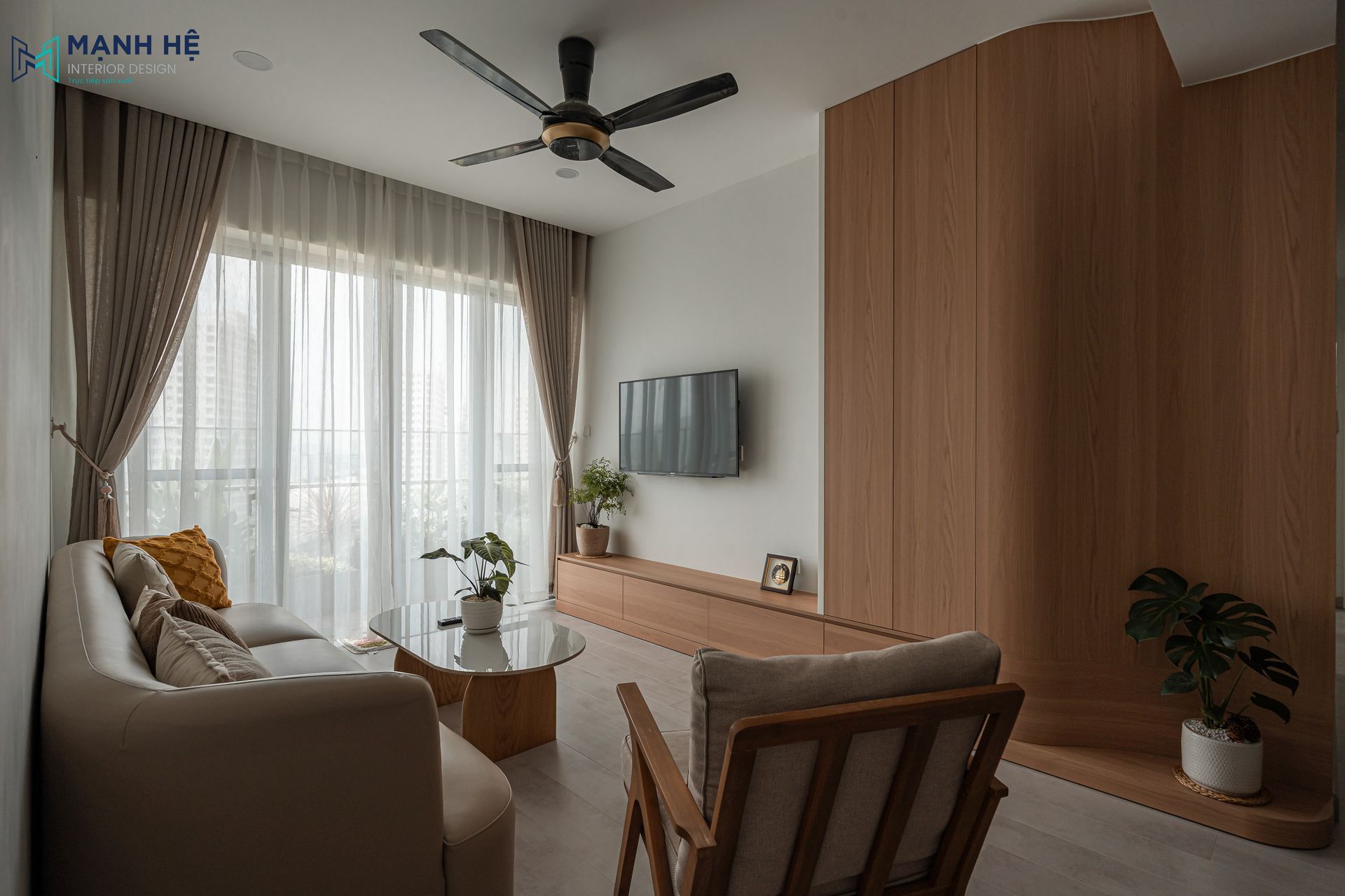 Hệ tủ tivi kết hợp vách ốp gỗ bo cong liền khối, giúp không gian phòng khách gọn gàng và an toàn khi sử dụng.