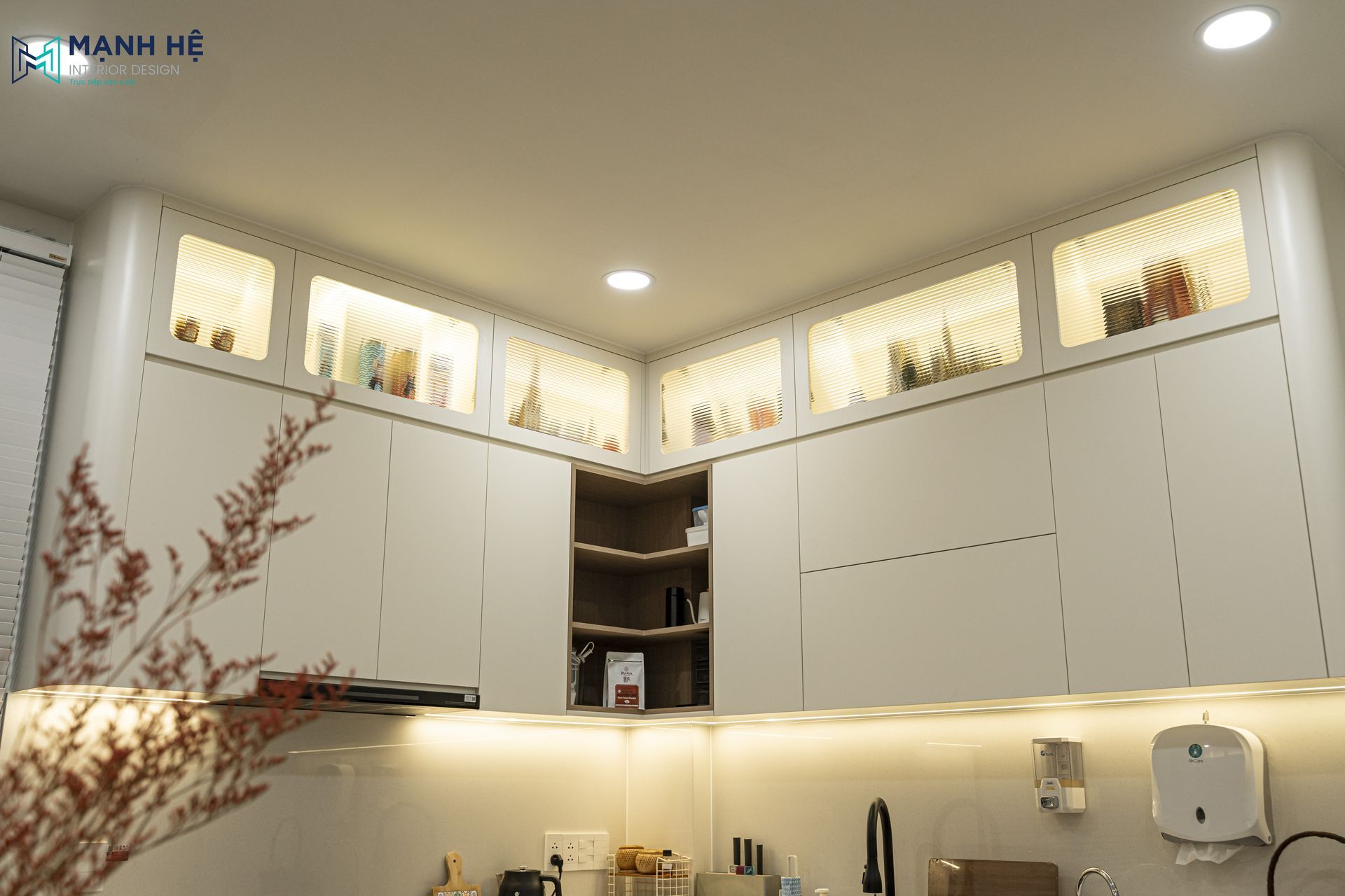 Thi công tủ bếp trên kịch trần phủ sơn trắng kem bo góc tròn mềm mại phối cánh kính sọc và đèn LED âm tủ.